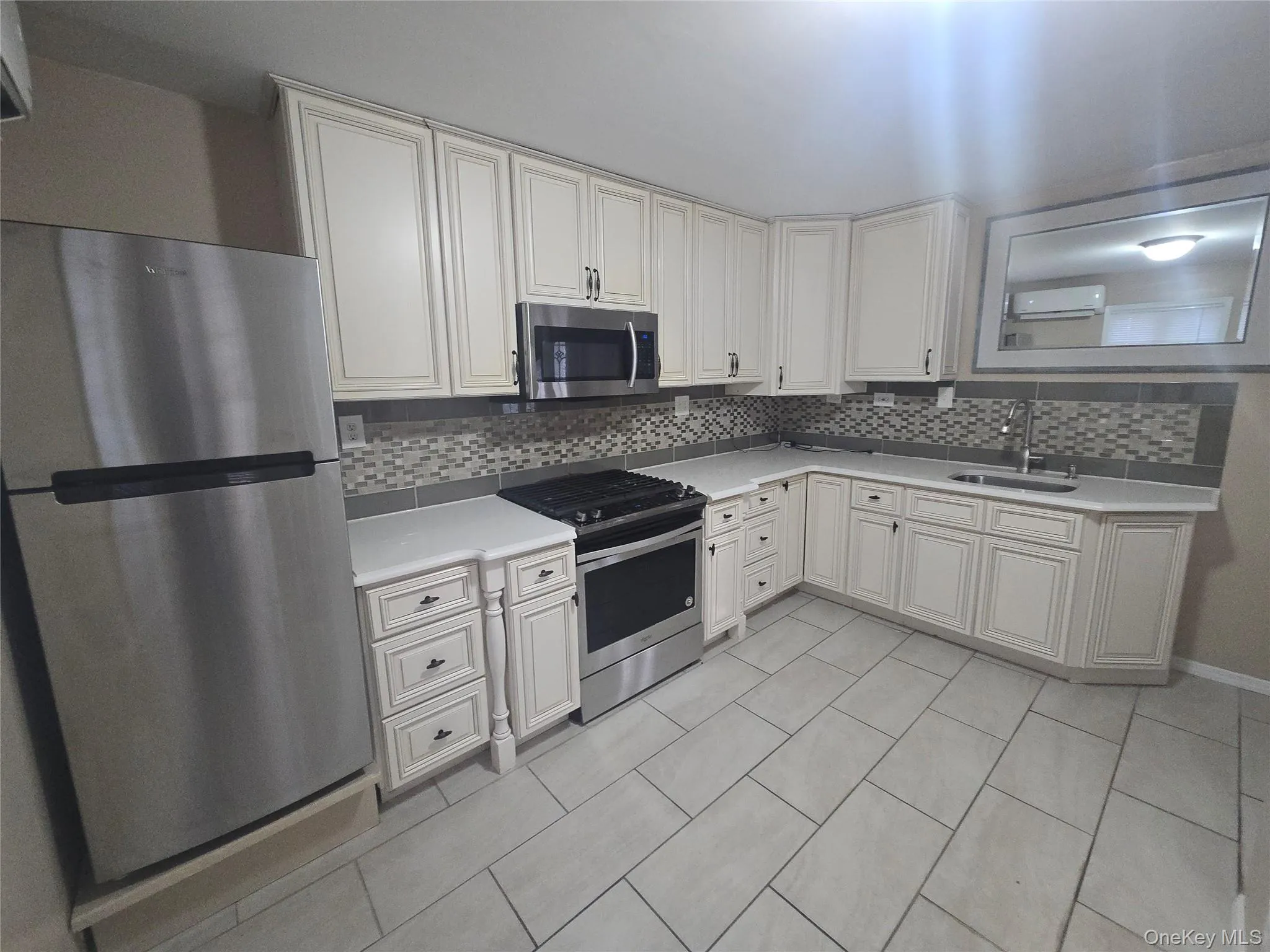 Kitchen featuring stainless steel appliances, decorative backsplash, an AC wall unit, and white cabinets Kitchen featuring stainless steel appliances, decorative backsplash, an AC wall unit, and white cabinets