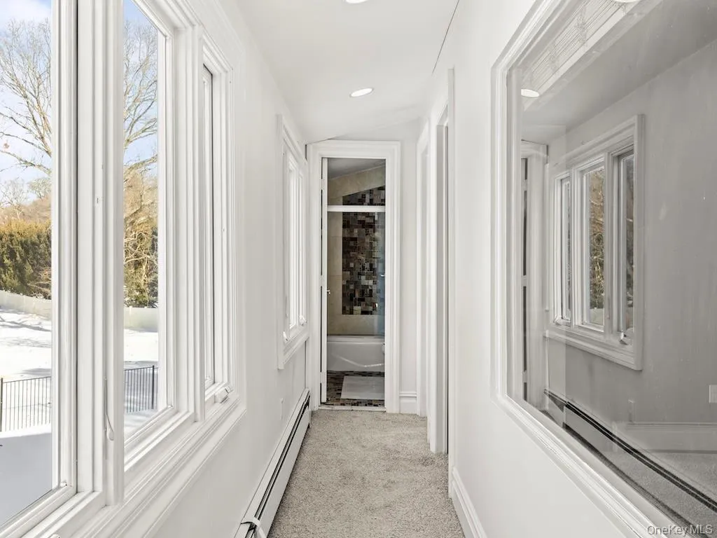 Hall with a baseboard radiator, a baseboard heating unit, light colored carpet, healthy amount of natural light, and recessed lighting Hall with a baseboard radiator, a baseboard heating unit, light colored carpet, healthy amount of natural light, and recessed lighting
