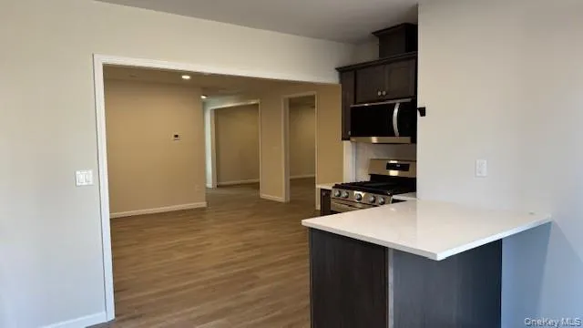 Kitchen featuring kitchen peninsula, appliances with stainless steel finishes, a kitchen bar, and dark wood-type flooring Kitchen featuring kitchen peninsula, appliances with stainless steel finishes, a kitchen bar, and dark wood-type flooring