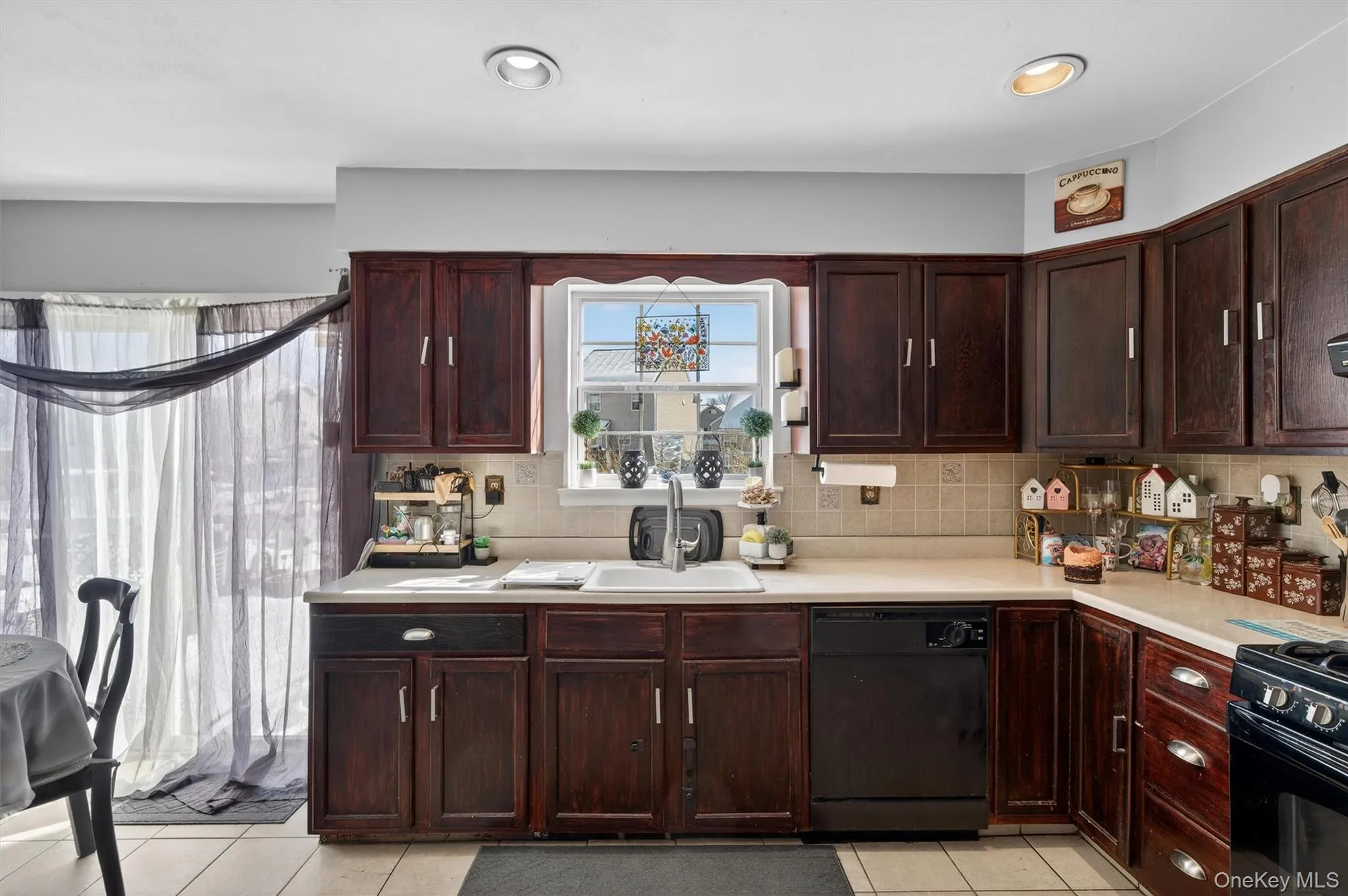 Kitchen with black appliances, light countertops, dark wood finish cabinetry, light tile patterned floors, and tasteful backsplash Kitchen with black appliances, light countertops, dark wood finish cabinetry, light tile patterned floors, and tasteful backsplash