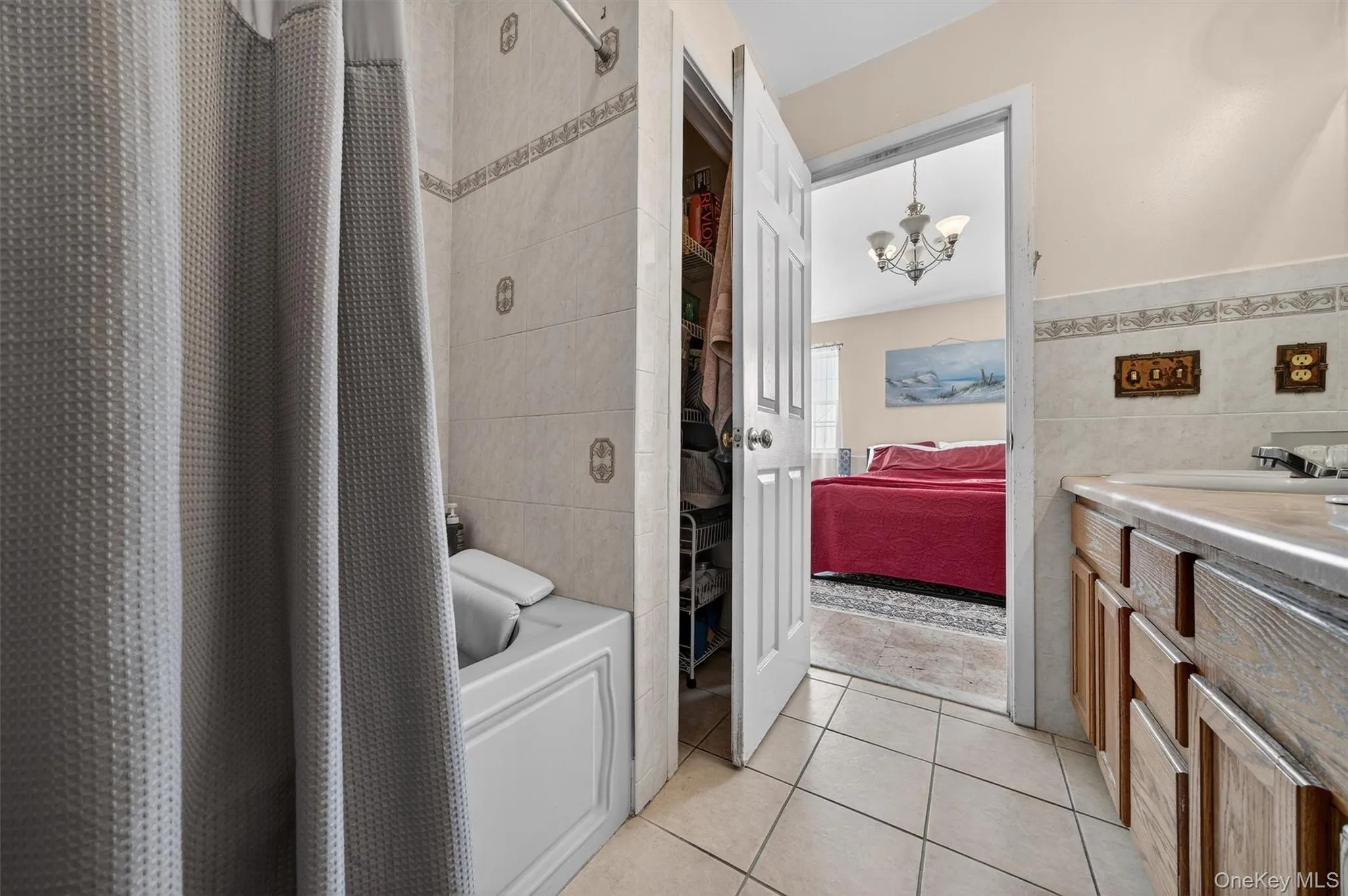 Ensuite bathroom with light tile patterned flooring, vanity, tile walls, suspended lighting, and shower / bath combination with curtain Ensuite bathroom with light tile patterned flooring, vanity, tile walls, suspended lighting, and shower / bath combination with curtain