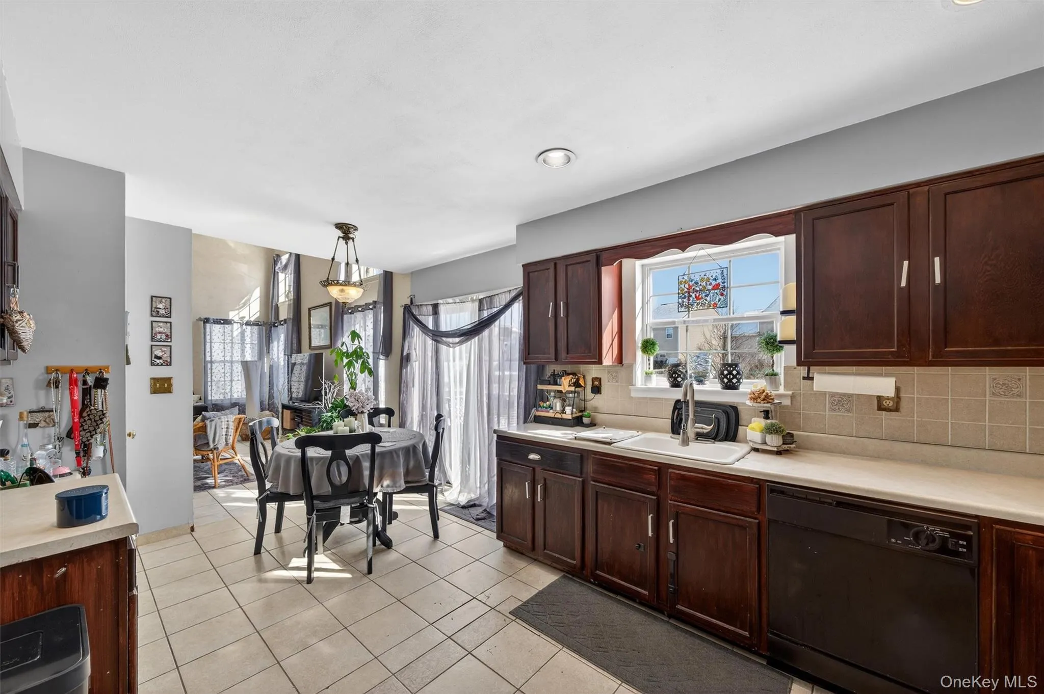 Kitchen with light countertops, dishwasher, dark wood finish cabinets, light tile patterned flooring, and decorative backsplash Kitchen with light countertops, dishwasher, dark wood finish cabinets, light tile patterned flooring, and decorative backsplash