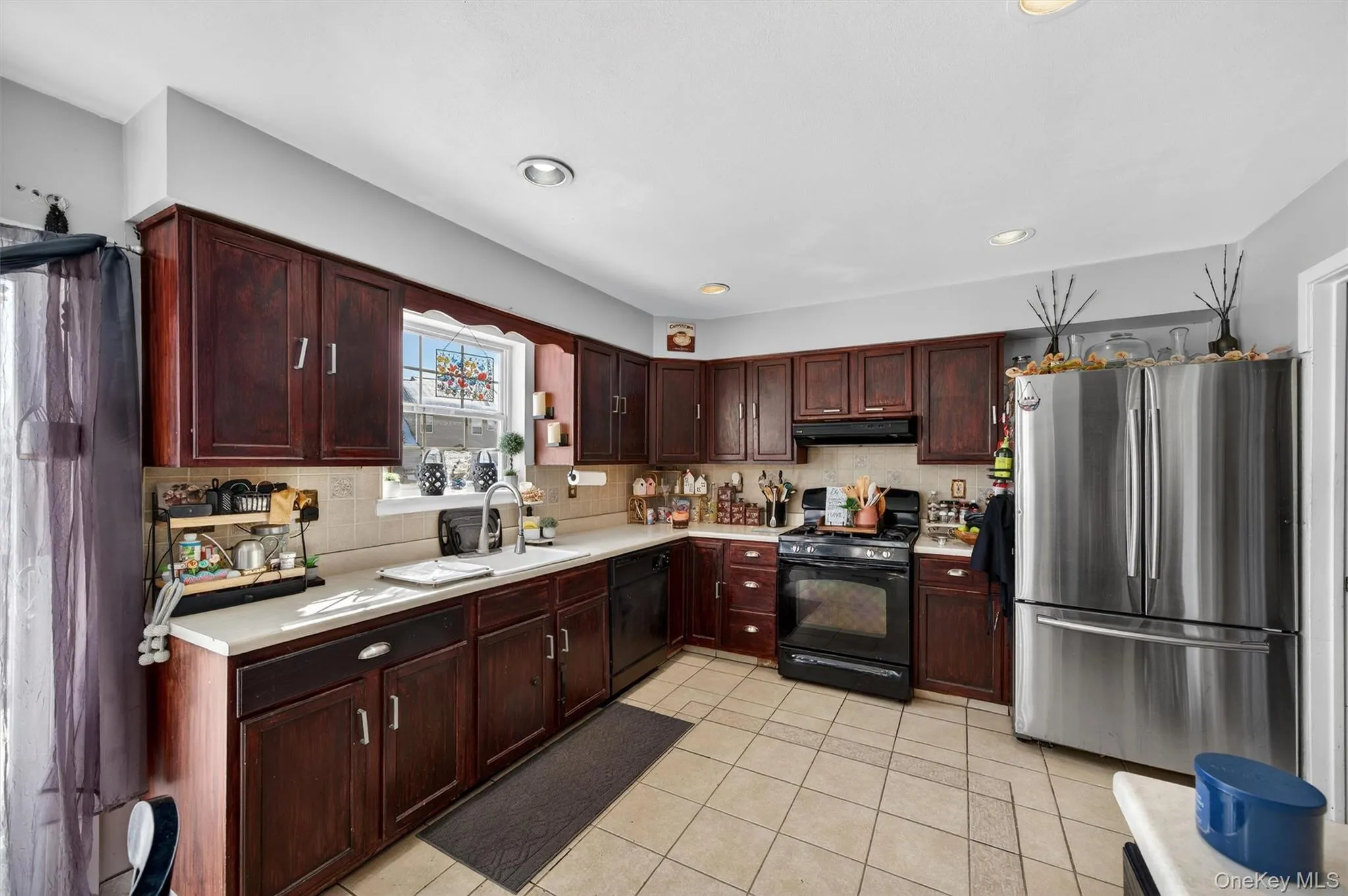 Kitchen featuring black appliances, light countertops, dark wood finish cabinets, decorative backsplash, and light tile patterned floors Kitchen featuring black appliances, light countertops, dark wood finish cabinets, decorative backsplash, and light tile patterned floors