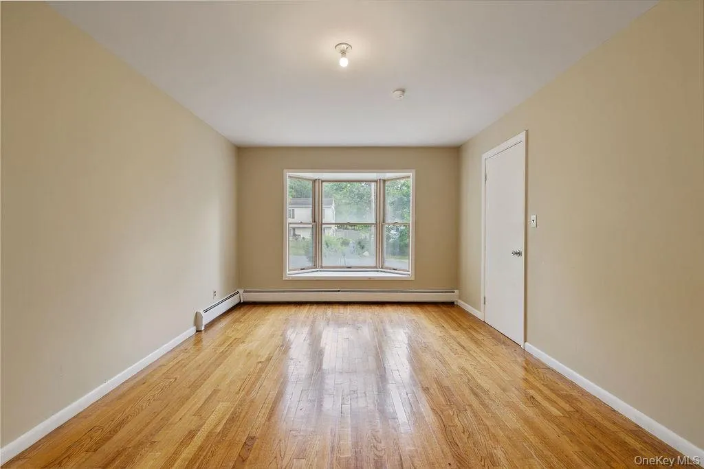 Unfurnished room with light wood-type flooring and a baseboard radiator Unfurnished room with light wood-type flooring and a baseboard radiator