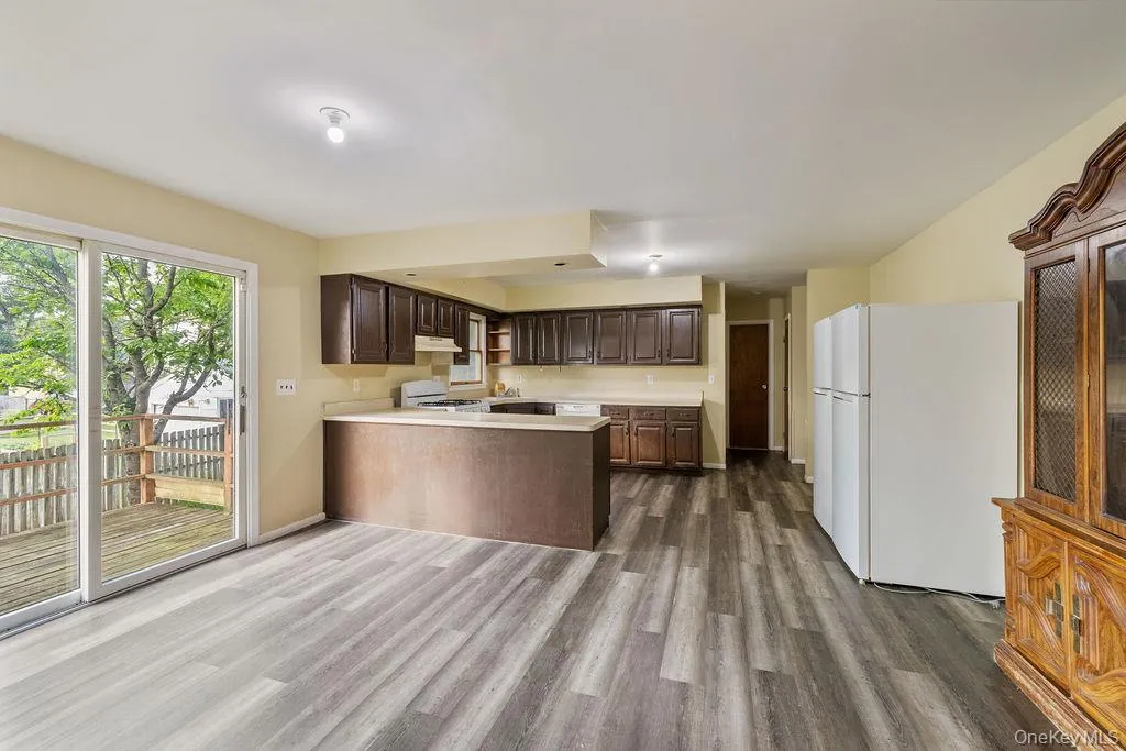 Kitchen with dark wood finish cabinetry, light countertops, white appliances, a peninsula, and dark wood-type flooring Kitchen with dark wood finish cabinetry, light countertops, white appliances, a peninsula, and dark wood-type flooring