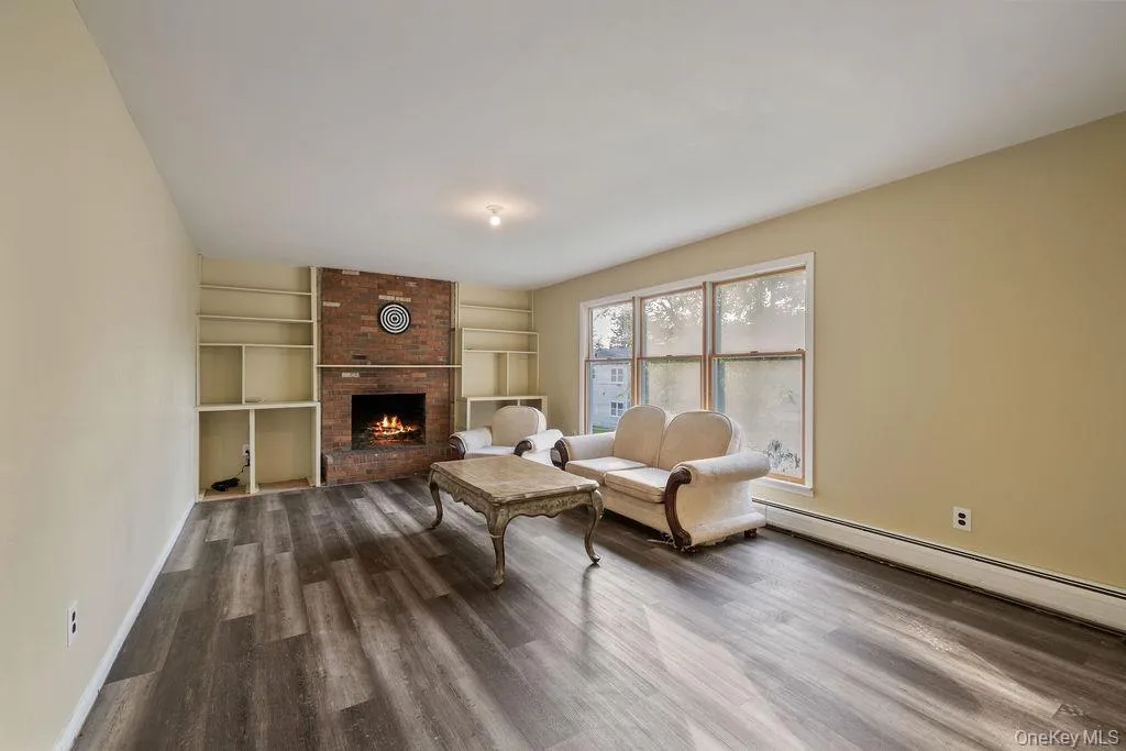 Living area featuring dark wood finished floors, a brick fireplace, and a baseboard radiator Living area featuring dark wood finished floors, a brick fireplace, and a baseboard radiator