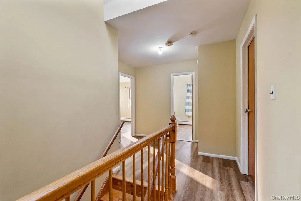 Corridor featuring an upstairs landing, wood finished floors, and a baseboard radiator Corridor featuring an upstairs landing, wood finished floors, and a baseboard radiator