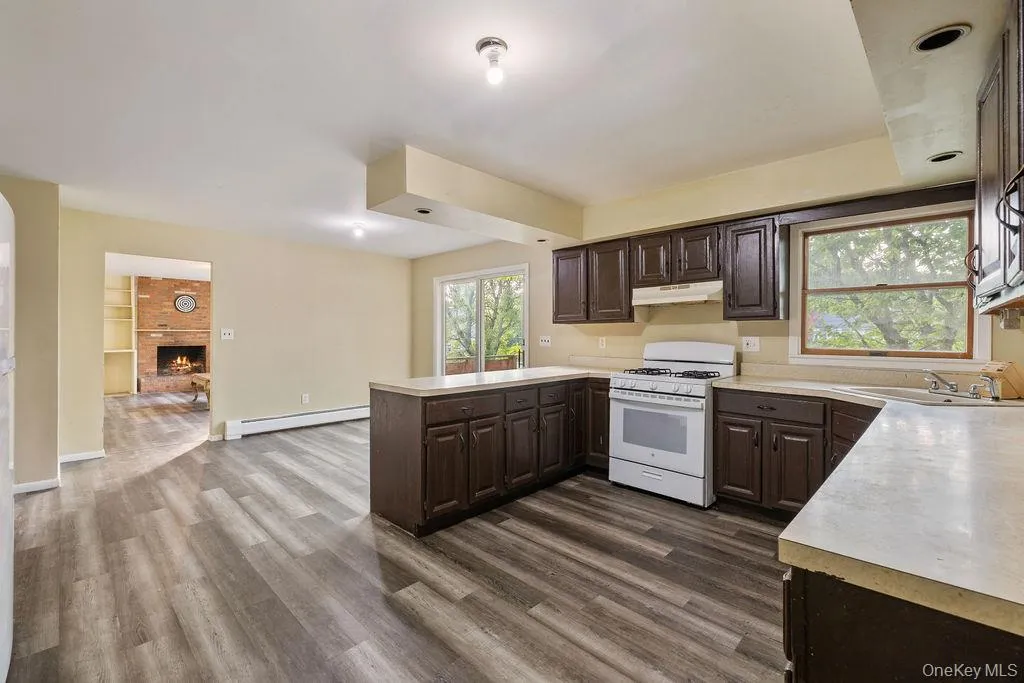 Kitchen featuring dark wood finish cabinets, light countertops, white gas stove, a peninsula, and dark wood finished floors Kitchen featuring dark wood finish cabinets, light countertops, white gas stove, a peninsula, and dark wood finished floors