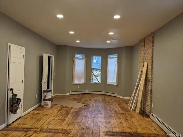 Empty room with a baseboard radiator, light wood finished floors, recessed lighting, and brick wall Empty room with a baseboard radiator, light wood finished floors, recessed lighting, and brick wall