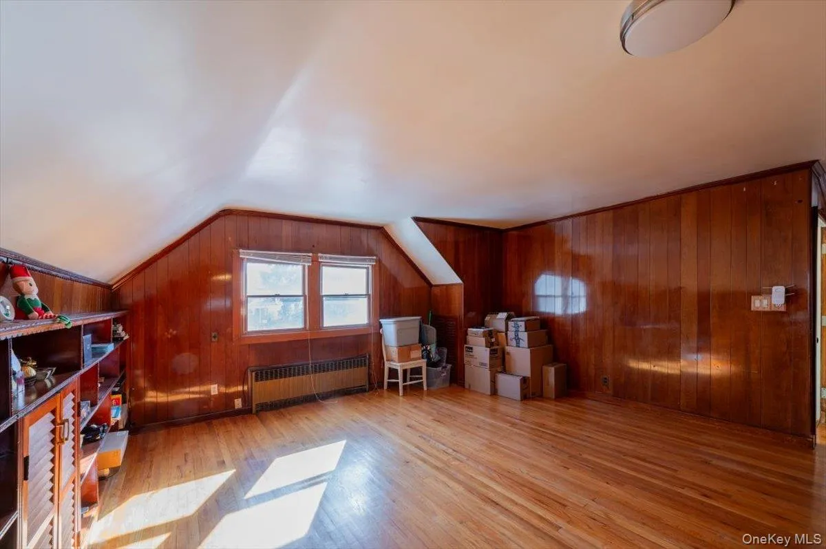 Bonus room featuring radiator heating unit, vaulted ceiling, wood walls, and wood finished floors Bonus room featuring radiator heating unit, vaulted ceiling, wood walls, and wood finished floors