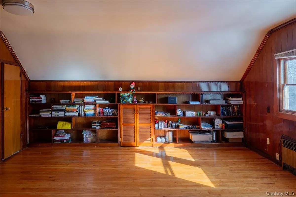 Office space with vaulted ceiling, radiator heating unit, wooden walls, and wood finished floors Office space with vaulted ceiling, radiator heating unit, wooden walls, and wood finished floors