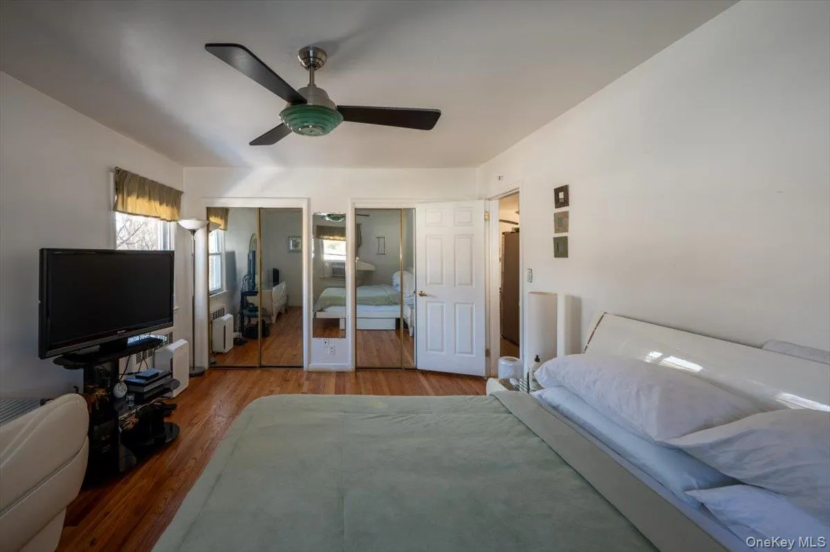 Bedroom with multiple closets, wood finished floors, radiator heating unit, and a ceiling fan Bedroom with multiple closets, wood finished floors, radiator heating unit, and a ceiling fan