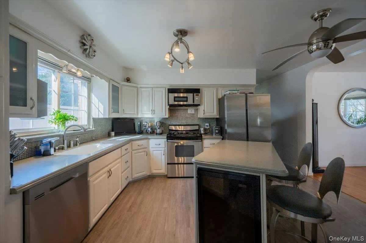 Kitchen featuring appliances with stainless steel finishes, a breakfast bar area, backsplash, light wood finished floors, and glass insert cabinets Kitchen featuring appliances with stainless steel finishes, a breakfast bar area, backsplash, light wood finished floors, and glass insert cabinets