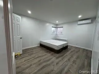 Bedroom with an AC wall unit, recessed lighting, wood finished floors, and baseboards Bedroom with an AC wall unit, recessed lighting, wood finished floors, and baseboards