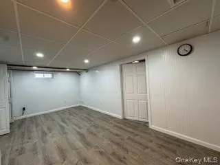 Finished basement featuring baseboards, a paneled ceiling, and wood finished floors Finished basement featuring baseboards, a paneled ceiling, and wood finished floors