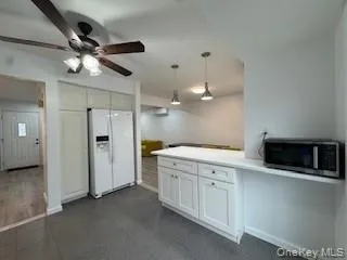 Kitchen with a ceiling fan, stainless steel microwave, white refrigerator with ice dispenser, white cabinets, and hanging light fixtures Kitchen with a ceiling fan, stainless steel microwave, white refrigerator with ice dispenser, white cabinets, and hanging light fixtures