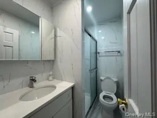 Bathroom featuring vanity, stone wall, toilet, and a marble finish shower Bathroom featuring vanity, stone wall, toilet, and a marble finish shower