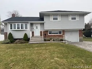 Split level home featuring a front yard, an attached garage, brick siding, and driveway Split level home featuring a front yard, an attached garage, brick siding, and driveway