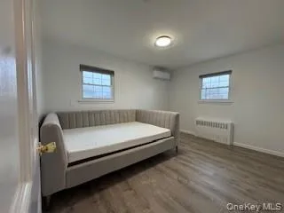 Bedroom with a wall mounted air conditioner, baseboards, wood finished floors, and radiator heating unit Bedroom with a wall mounted air conditioner, baseboards, wood finished floors, and radiator heating unit