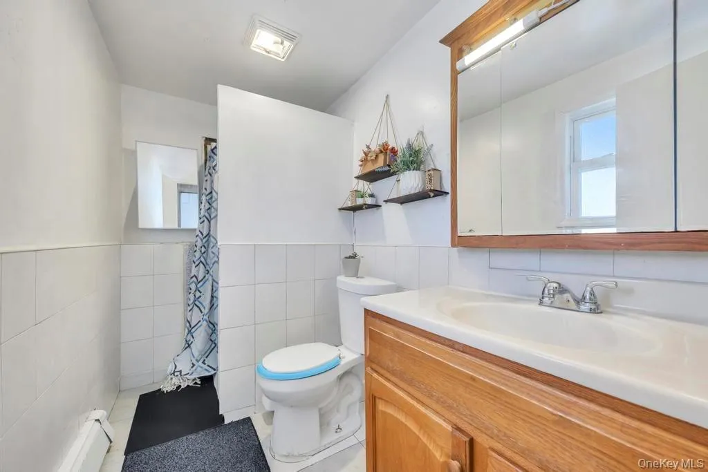 Bathroom featuring vanity, tile walls, a shower with shower curtain, a baseboard heating unit, and light tile patterned floors Bathroom featuring vanity, tile walls, a shower with shower curtain, a baseboard heating unit, and light tile patterned floors