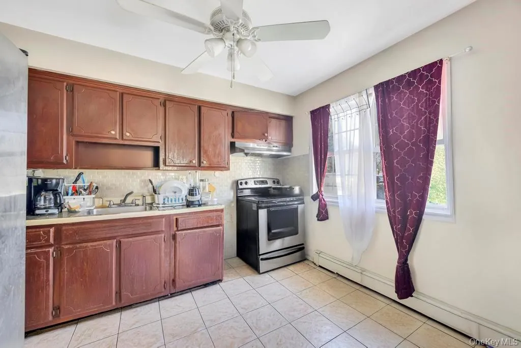 Kitchen with a baseboard radiator, light countertops, stainless steel electric range, a ceiling fan, and light tile patterned flooring Kitchen with a baseboard radiator, light countertops, stainless steel electric range, a ceiling fan, and light tile patterned flooring