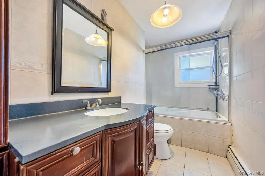 Bathroom featuring vanity, baseboard heating, tiled shower / bath combo, light tile patterned floors, and tile walls Bathroom featuring vanity, baseboard heating, tiled shower / bath combo, light tile patterned floors, and tile walls
