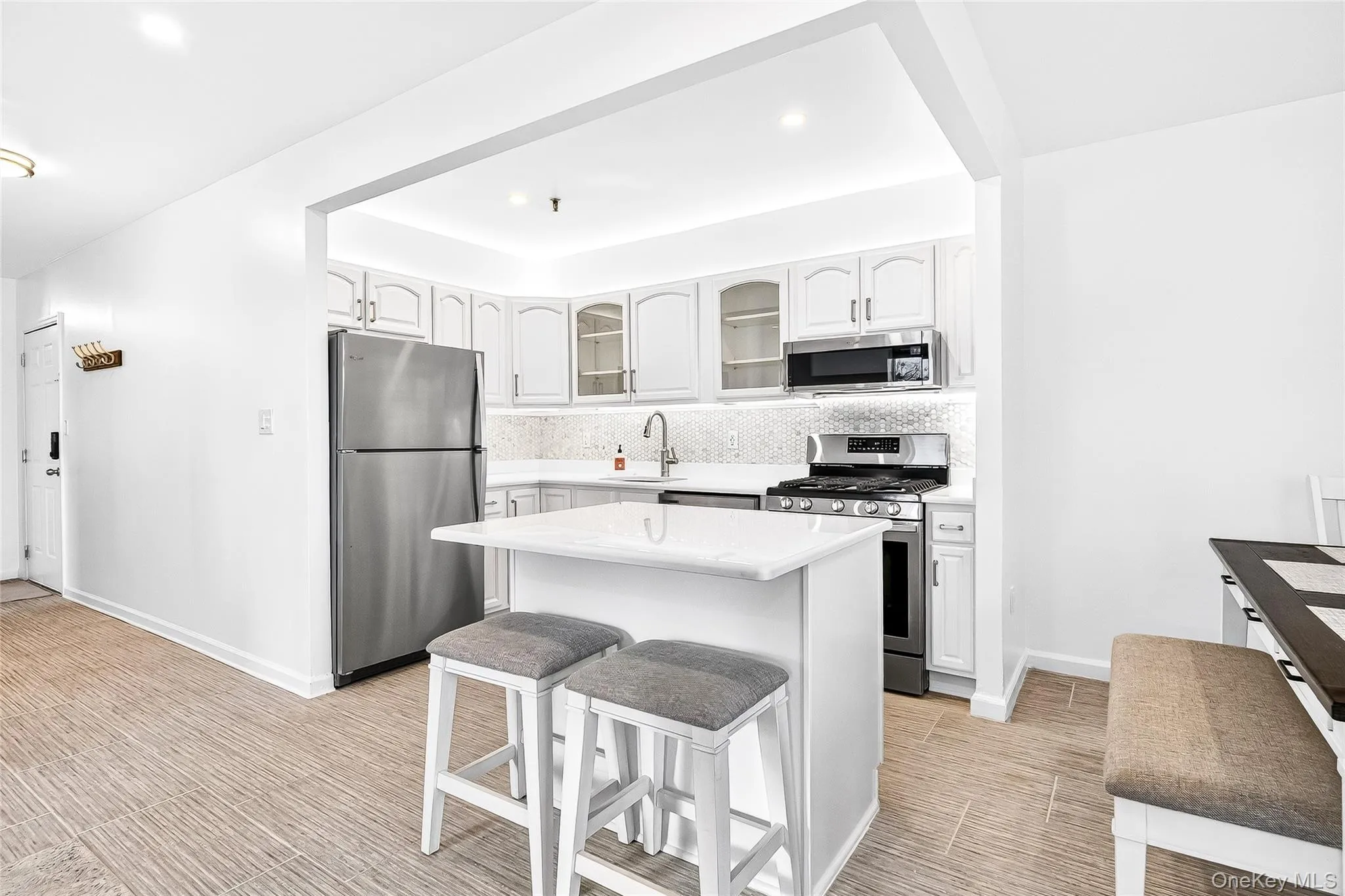Kitchen featuring a breakfast bar, stainless steel appliances, glass fronted cabinets, white cabinetry, and a kitchen island Kitchen featuring a breakfast bar, stainless steel appliances, glass fronted cabinets, white cabinetry, and a kitchen island