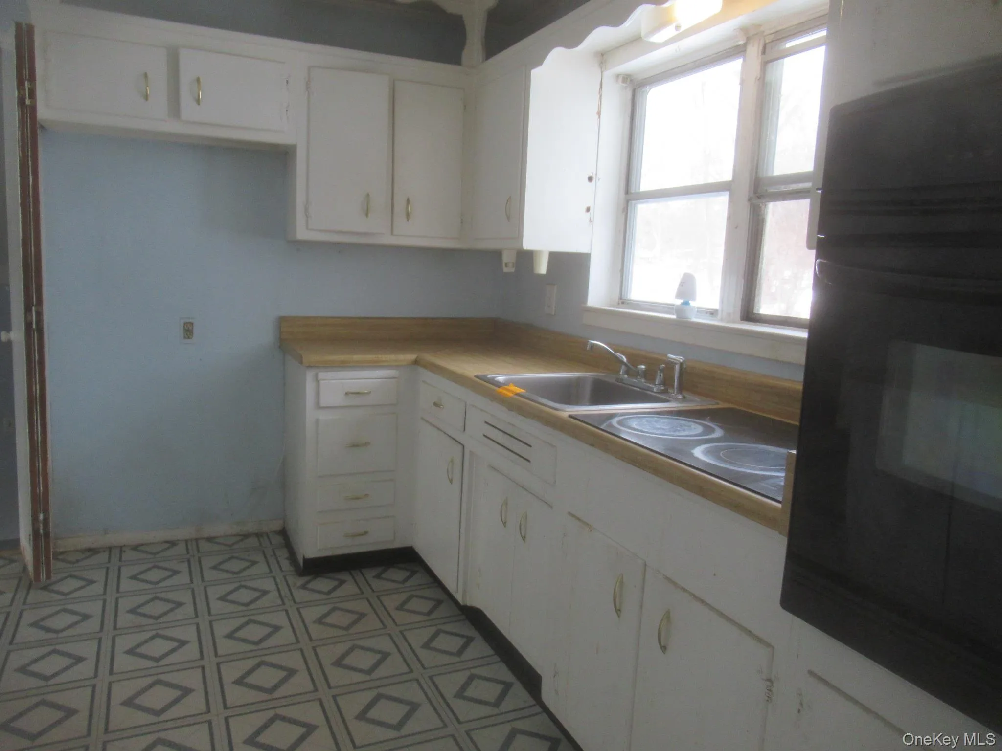 Kitchen featuring black oven, white cabinets, light countertops, and light floors Kitchen featuring black oven, white cabinets, light countertops, and light floors