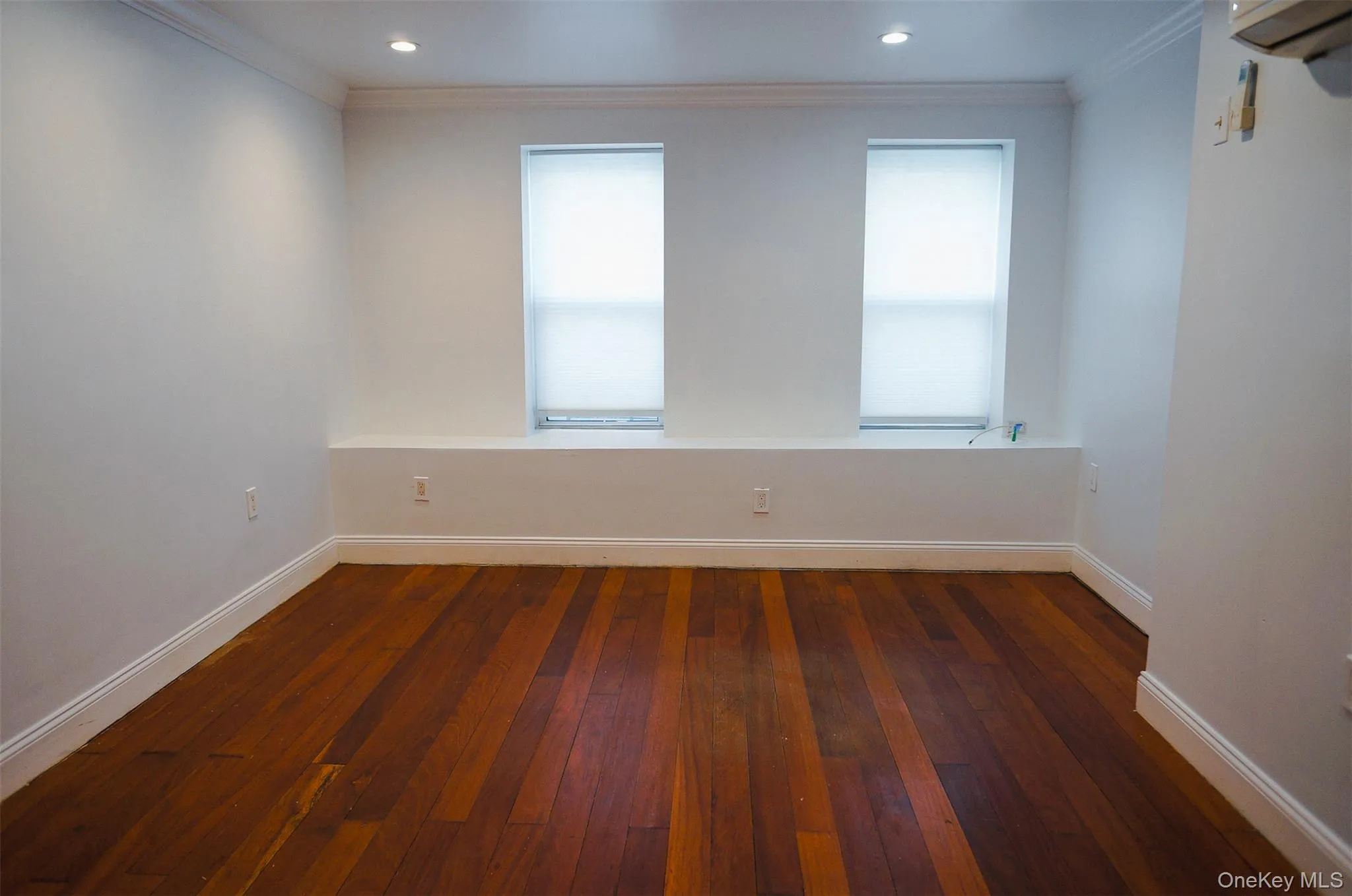 Unfurnished room with crown molding, dark wood-style floors, healthy amount of natural light, a wall mounted air conditioner/heater, and recessed lighting Unfurnished room with crown molding, dark wood-style floors, healthy amount of natural light, a wall mounted air conditioner/heater, and recessed lighting