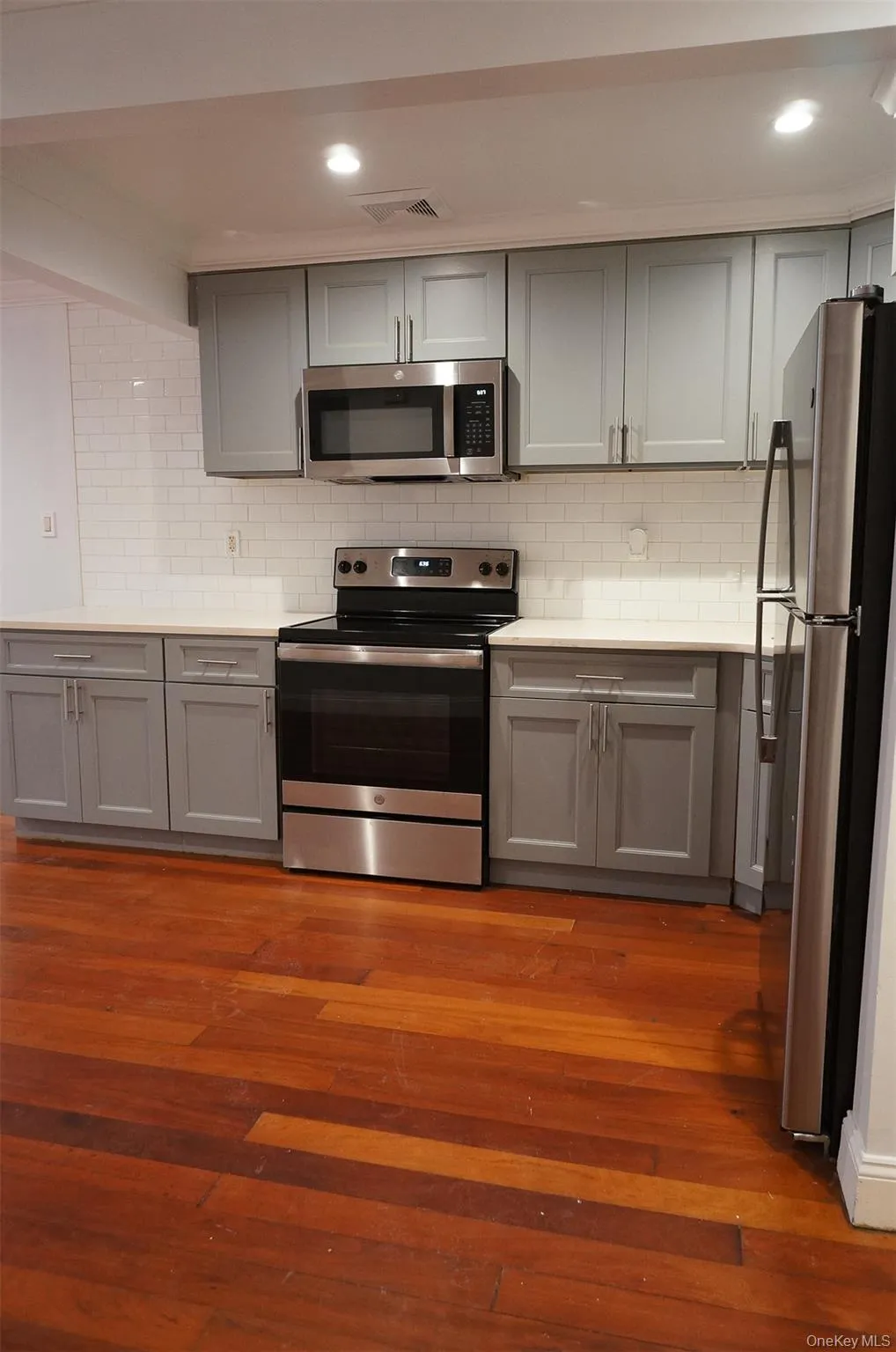Kitchen featuring gray cabinetry, stainless steel appliances, decorative backsplash, dark wood-type flooring, and recessed lighting Kitchen featuring gray cabinetry, stainless steel appliances, decorative backsplash, dark wood-type flooring, and recessed lighting