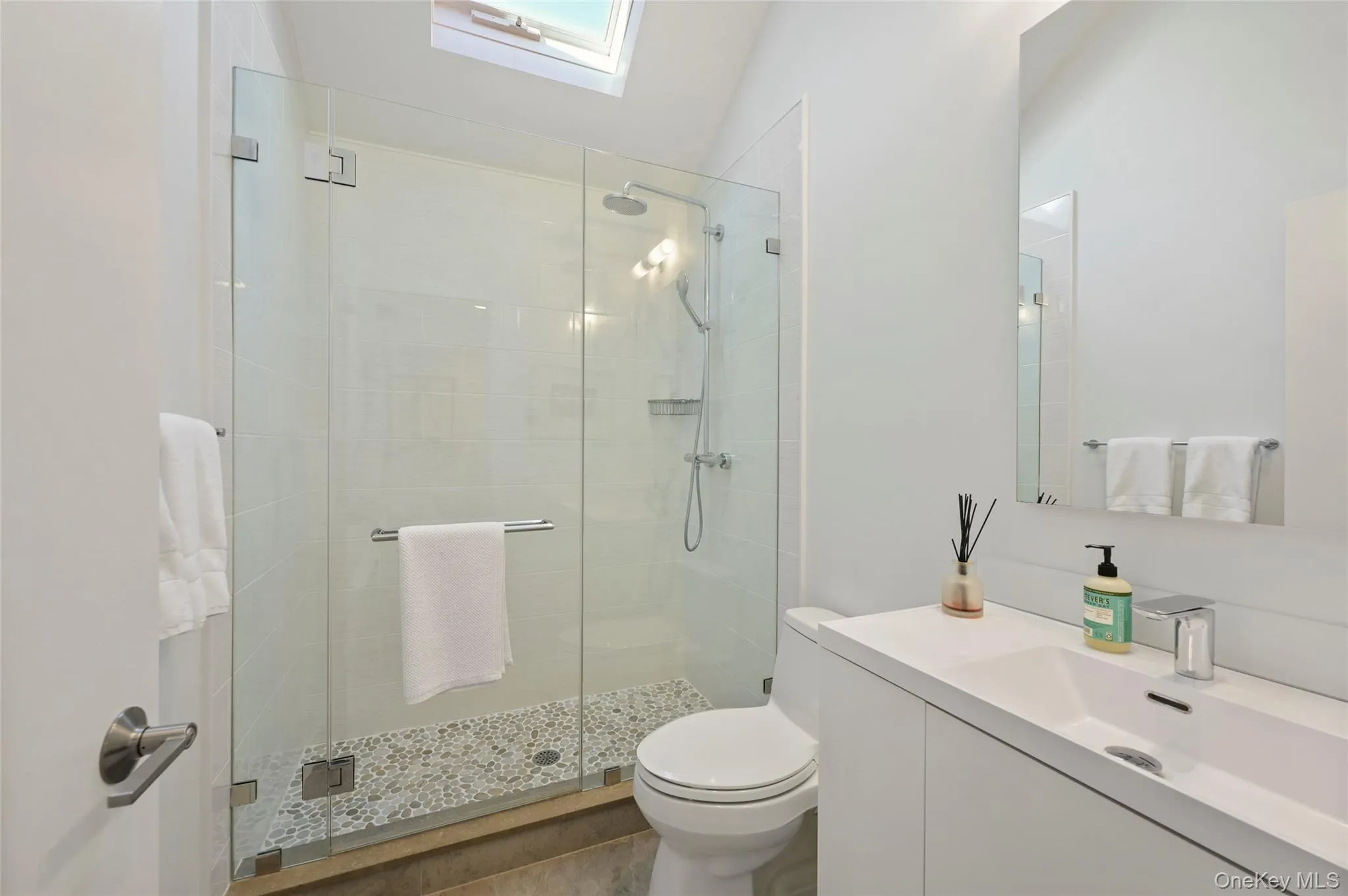 Bathroom with vaulted ceiling with skylight, vanity, toilet, and a shower with door Bathroom with vaulted ceiling with skylight, vanity, toilet, and a shower with door