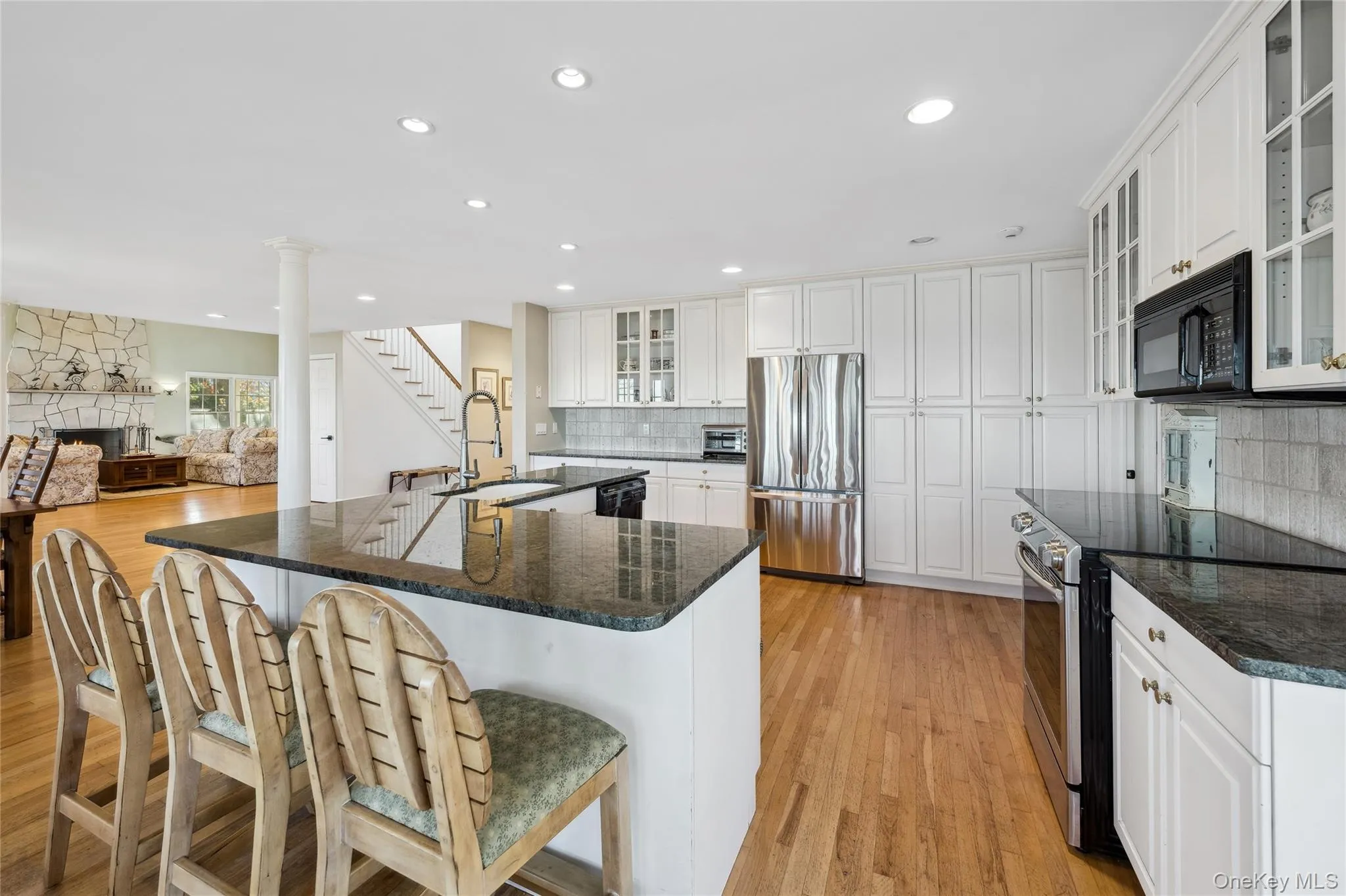 Kitchen featuring light wood finished floors, a stone fireplace, a sink, decorative backsplash, and black appliances Kitchen featuring light wood finished floors, a stone fireplace, a sink, decorative backsplash, and black appliances