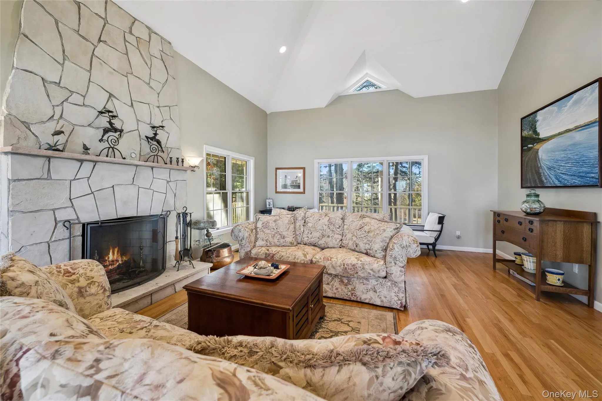 Living room with high vaulted ceiling, wood finished floors, a stone fireplace, baseboards, and visible vents Living room with high vaulted ceiling, wood finished floors, a stone fireplace, baseboards, and visible vents