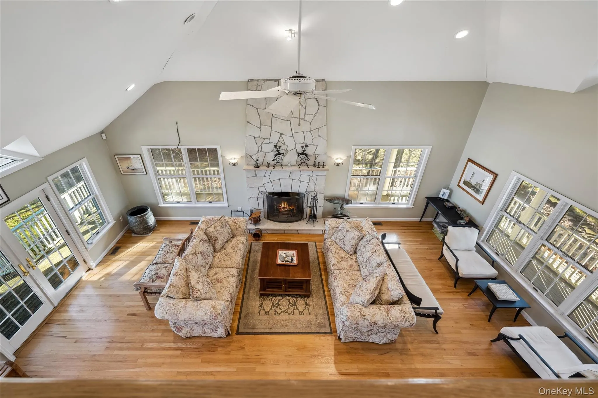 Living area with high vaulted ceiling, ceiling fan, wood finished floors, and a fireplace Living area with high vaulted ceiling, ceiling fan, wood finished floors, and a fireplace