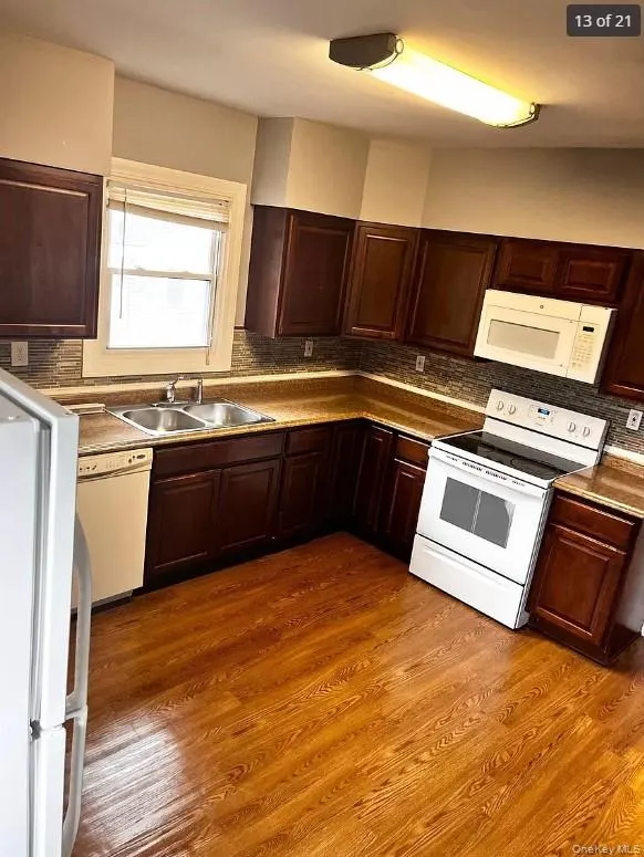 Kitchen with sink, wood-type flooring, tasteful backsplash, and white appliances Kitchen with sink, wood-type flooring, tasteful backsplash, and white appliances