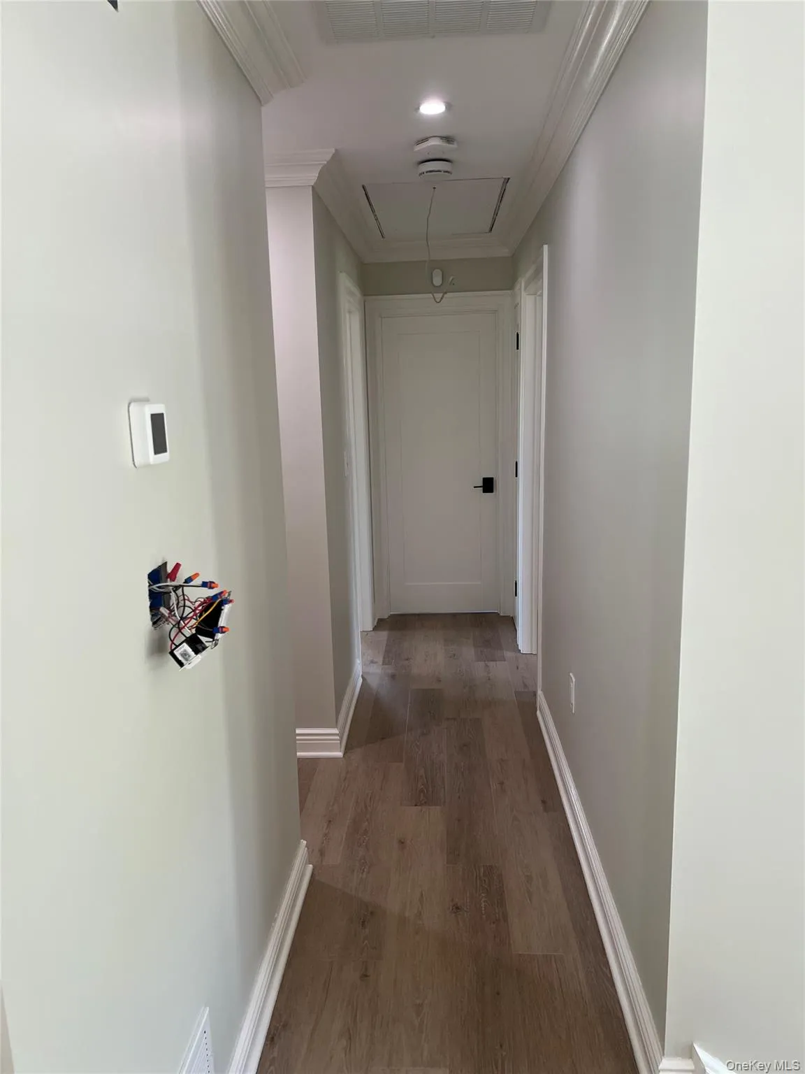 Hallway with attic access, ornamental molding, and wood finished floors Hallway with attic access, ornamental molding, and wood finished floors