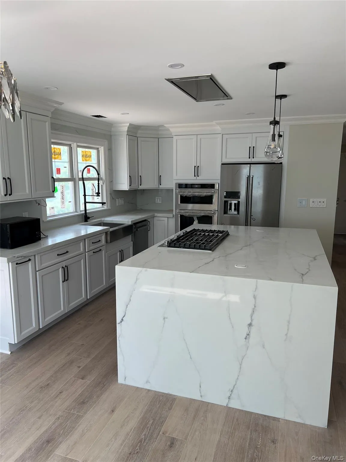 Kitchen with stainless steel appliances, a center island, decorative light fixtures, light wood-type flooring, and ornamental molding Kitchen with stainless steel appliances, a center island, decorative light fixtures, light wood-type flooring, and ornamental molding
