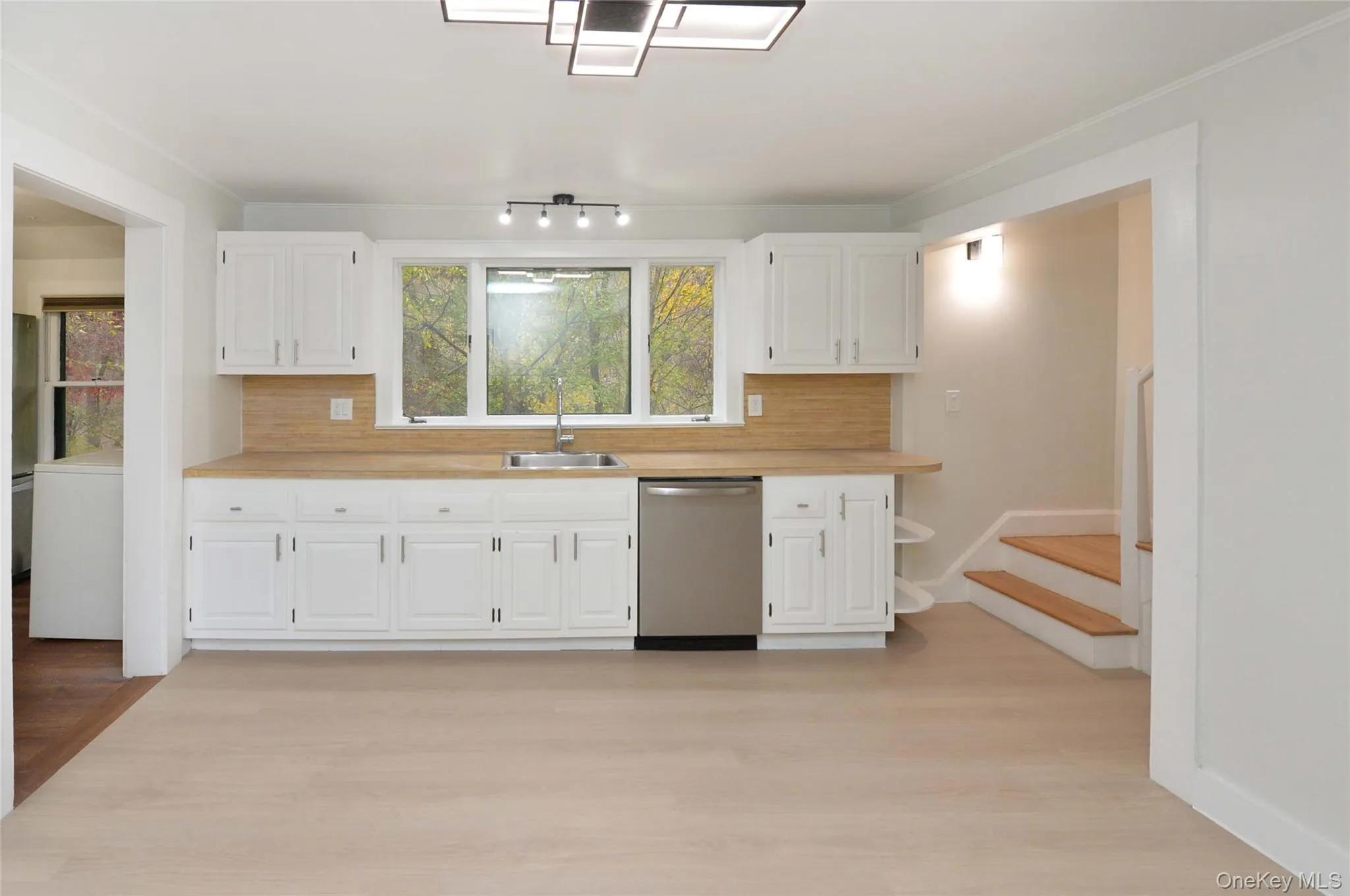 Kitchen with light countertops, stainless steel dishwasher, backsplash, and light wood finished floors Kitchen with light countertops, stainless steel dishwasher, backsplash, and light wood finished floors