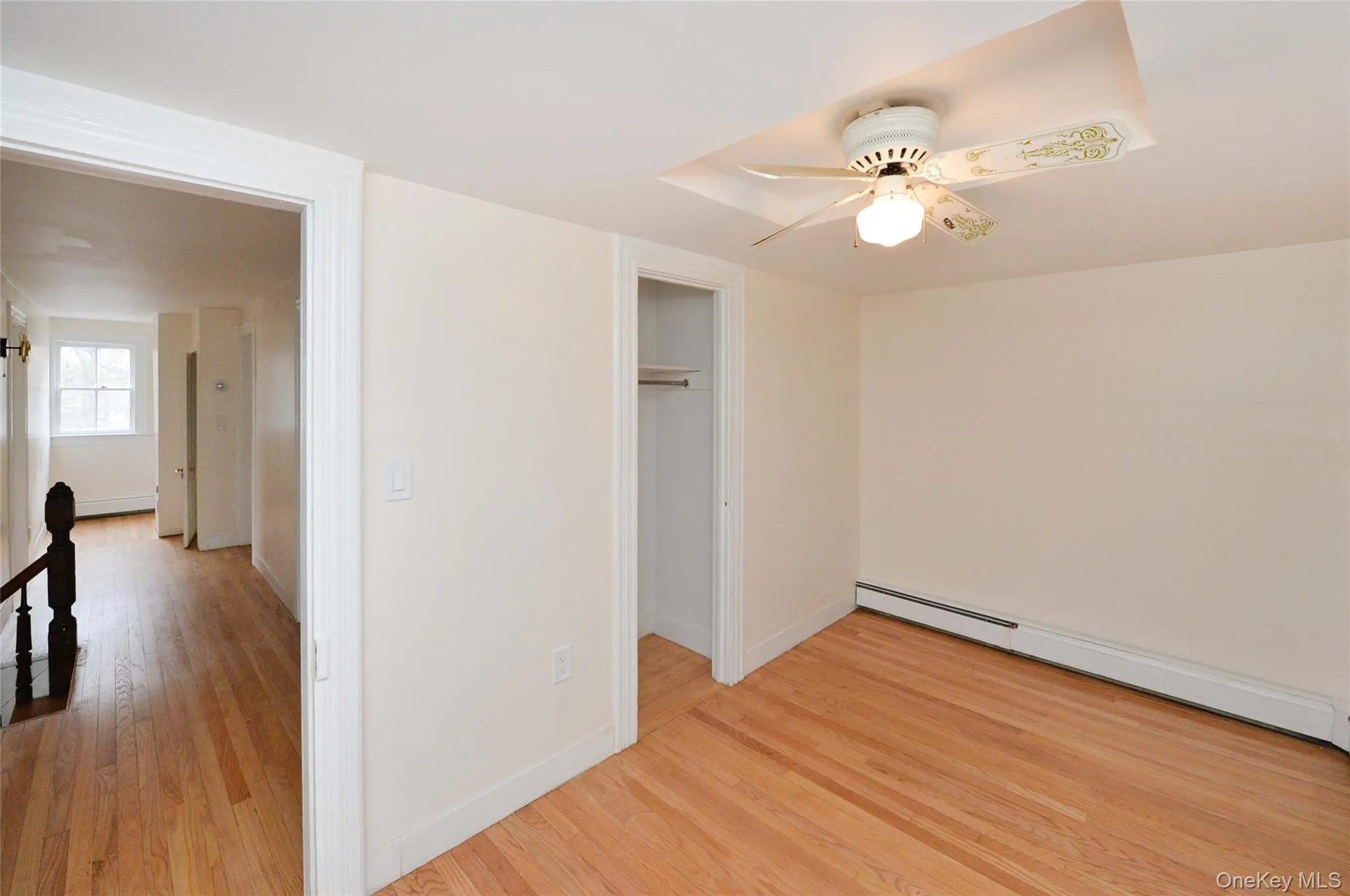 Unfurnished bedroom with light wood-style floors, ceiling fan, a baseboard radiator, and a baseboard heating unit Unfurnished bedroom with light wood-style floors, ceiling fan, a baseboard radiator, and a baseboard heating unit
