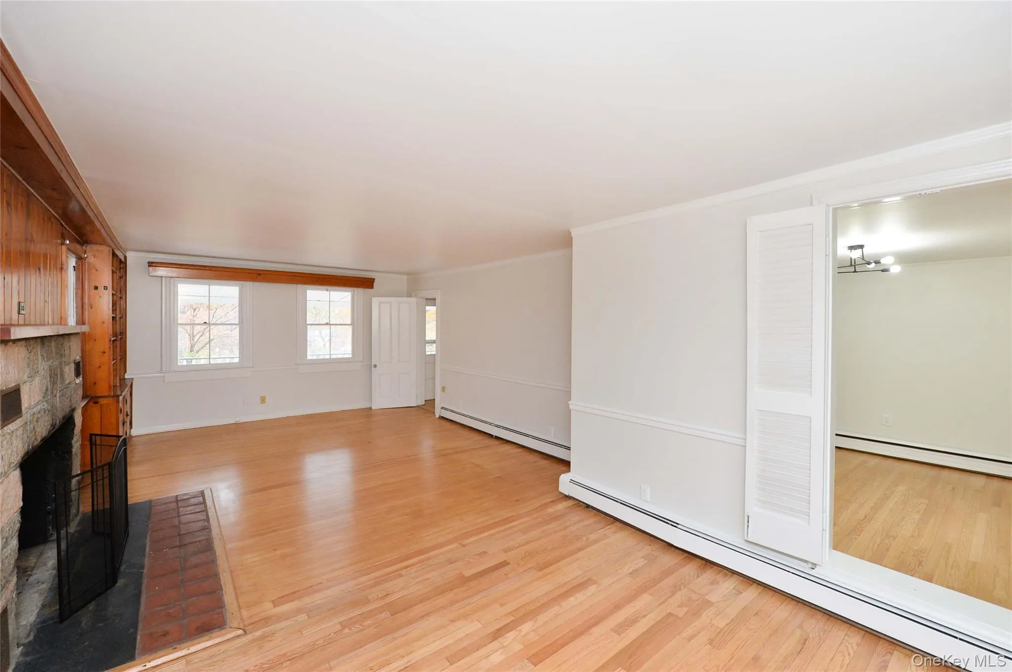Unfurnished living room featuring a baseboard heating unit, a brick fireplace, light wood finished floors, and crown molding Unfurnished living room featuring a baseboard heating unit, a brick fireplace, light wood finished floors, and crown molding