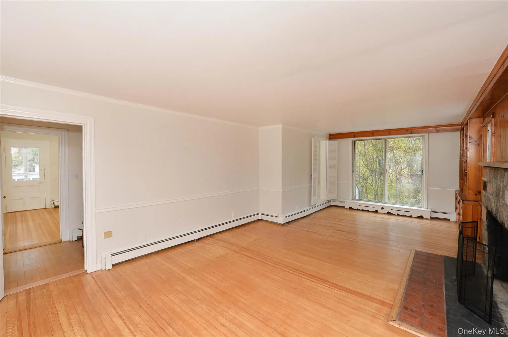 Unfurnished living room with plenty of natural light, light wood finished floors, a brick fireplace, a baseboard radiator, and crown molding Unfurnished living room with plenty of natural light, light wood finished floors, a brick fireplace, a baseboard radiator, and crown molding