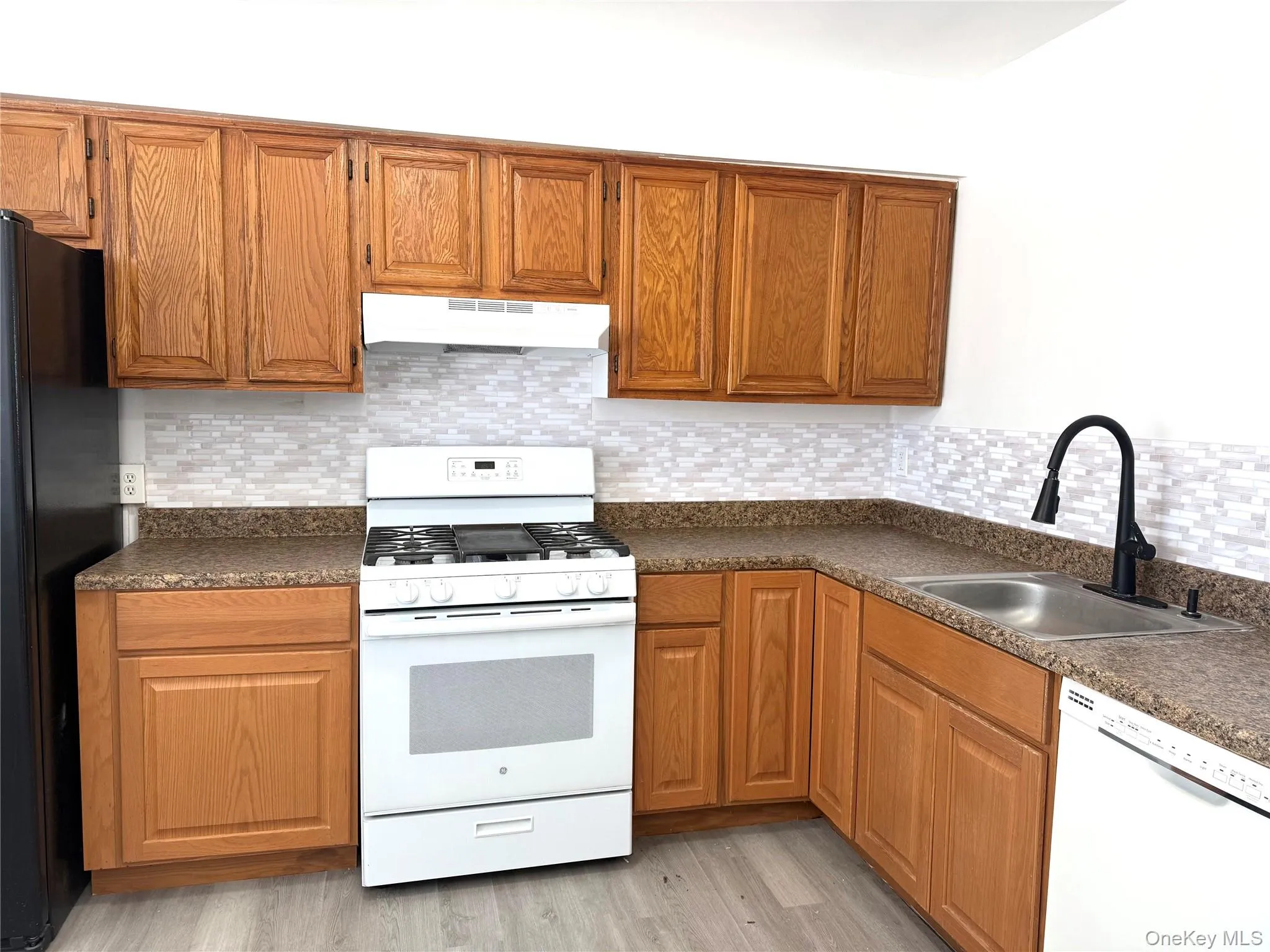 Kitchen with white appliances, dark countertops, wood finish cabinets, and backsplash Kitchen with white appliances, dark countertops, wood finish cabinets, and backsplash