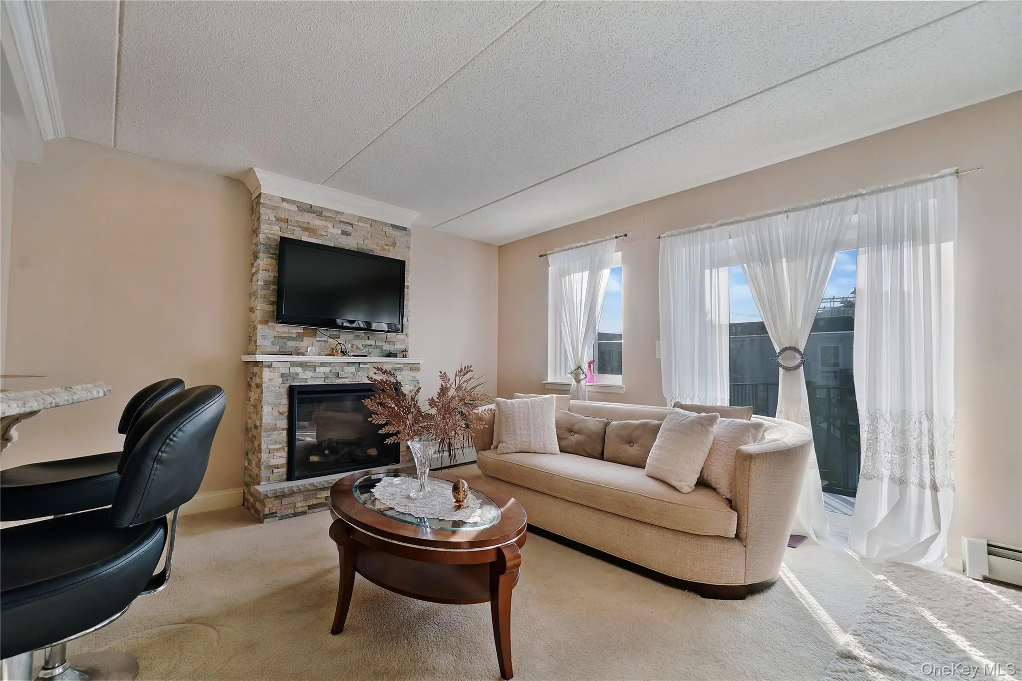 Living area featuring a floor-to-ceiling stacked stone fireplace, an inset electric fireplace, and a wall-mounted television Living area featuring a floor-to-ceiling stacked stone fireplace, an inset electric fireplace, and a wall-mounted television