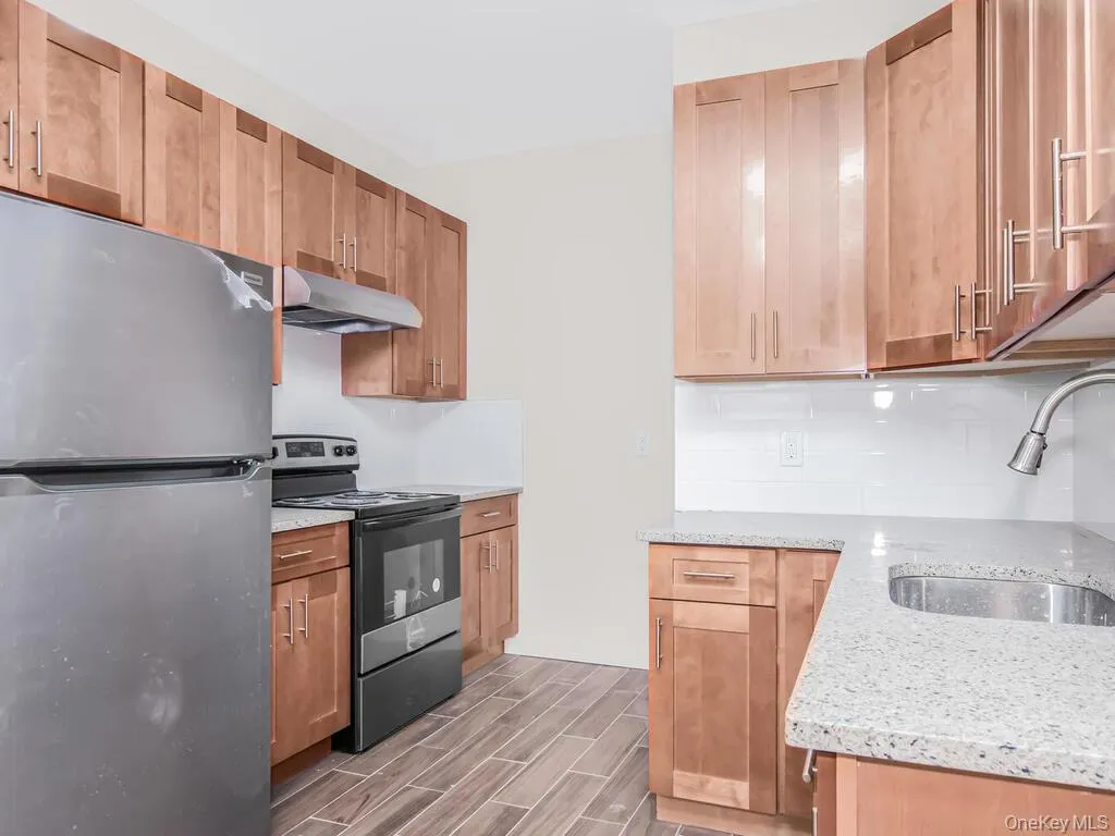 Kitchen featuring appliances with stainless steel finishes, light stone countertops, wood finish floors, and under cabinet range hood Kitchen featuring appliances with stainless steel finishes, light stone countertops, wood finish floors, and under cabinet range hood
