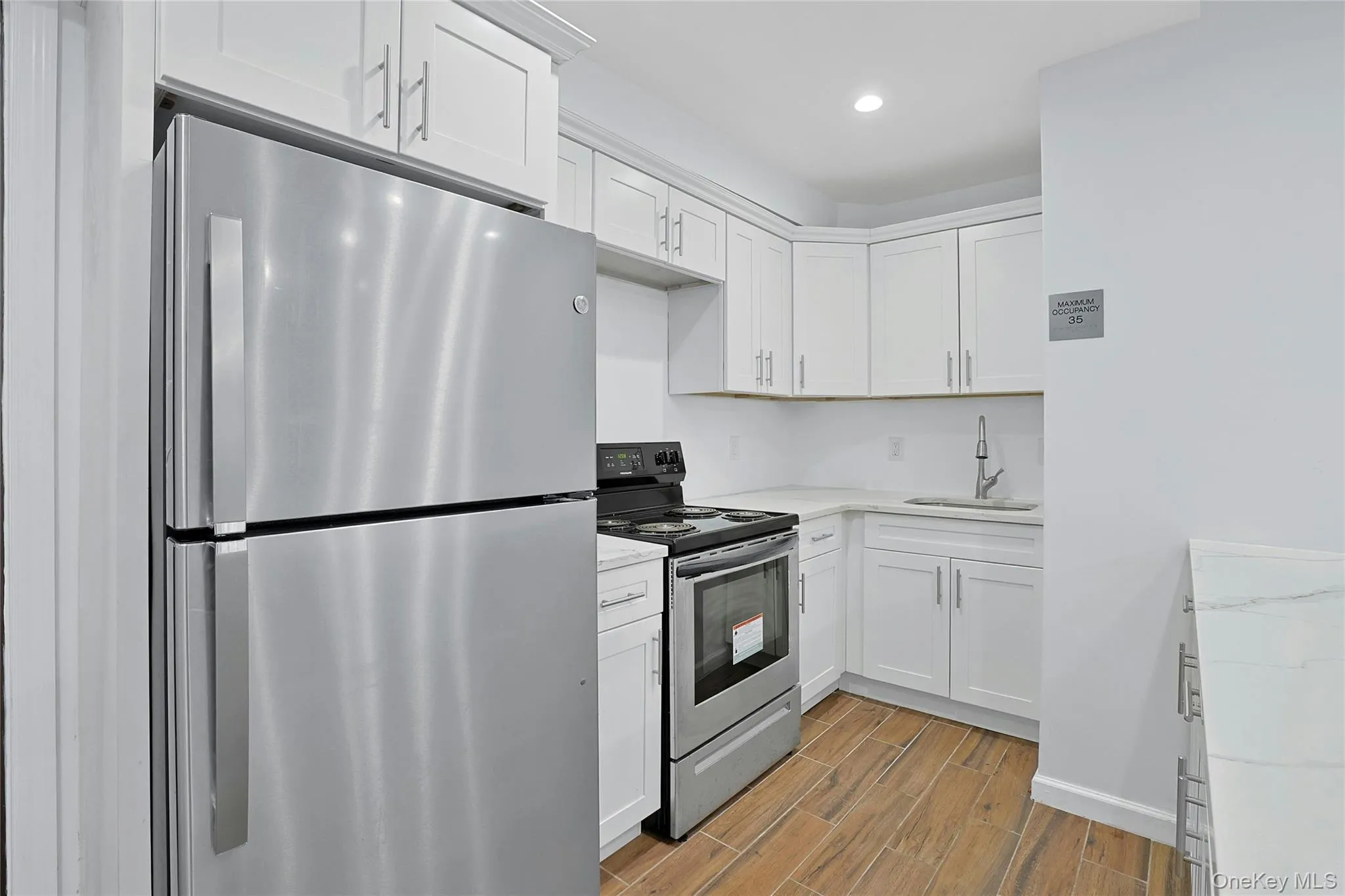 Community view 2 Renovated Kitchen with appliances with stainless steel finishes, white cabinets, wood finish floors, light stone counters, and recessed lighting Community view 2 Renovated Kitchen with appliances with stainless steel finishes, white cabinets, wood finish floors, light stone counters, and recessed lighting