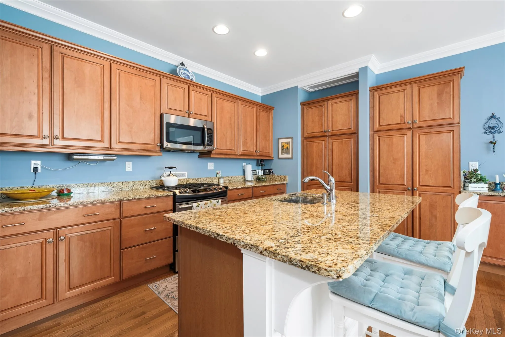 Kitchen with wood finish cabinets, light wood-type flooring, light stone countertops, stainless steel appliances, and ornamental molding Kitchen with wood finish cabinets, light wood-type flooring, light stone countertops, stainless steel appliances, and ornamental molding