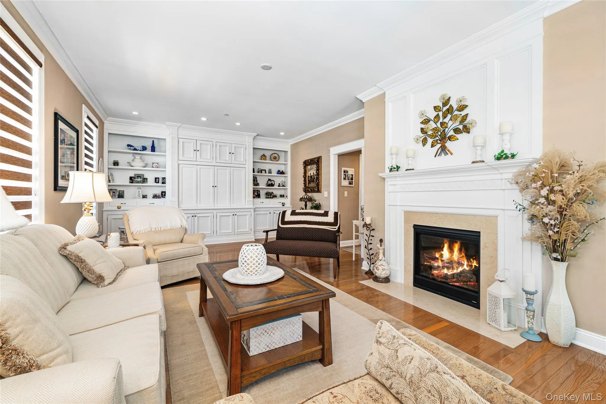 Living area featuring wood finished floors, built in shelves, crown molding, a high end fireplace, and recessed lighting Living area featuring wood finished floors, built in shelves, crown molding, a high end fireplace, and recessed lighting