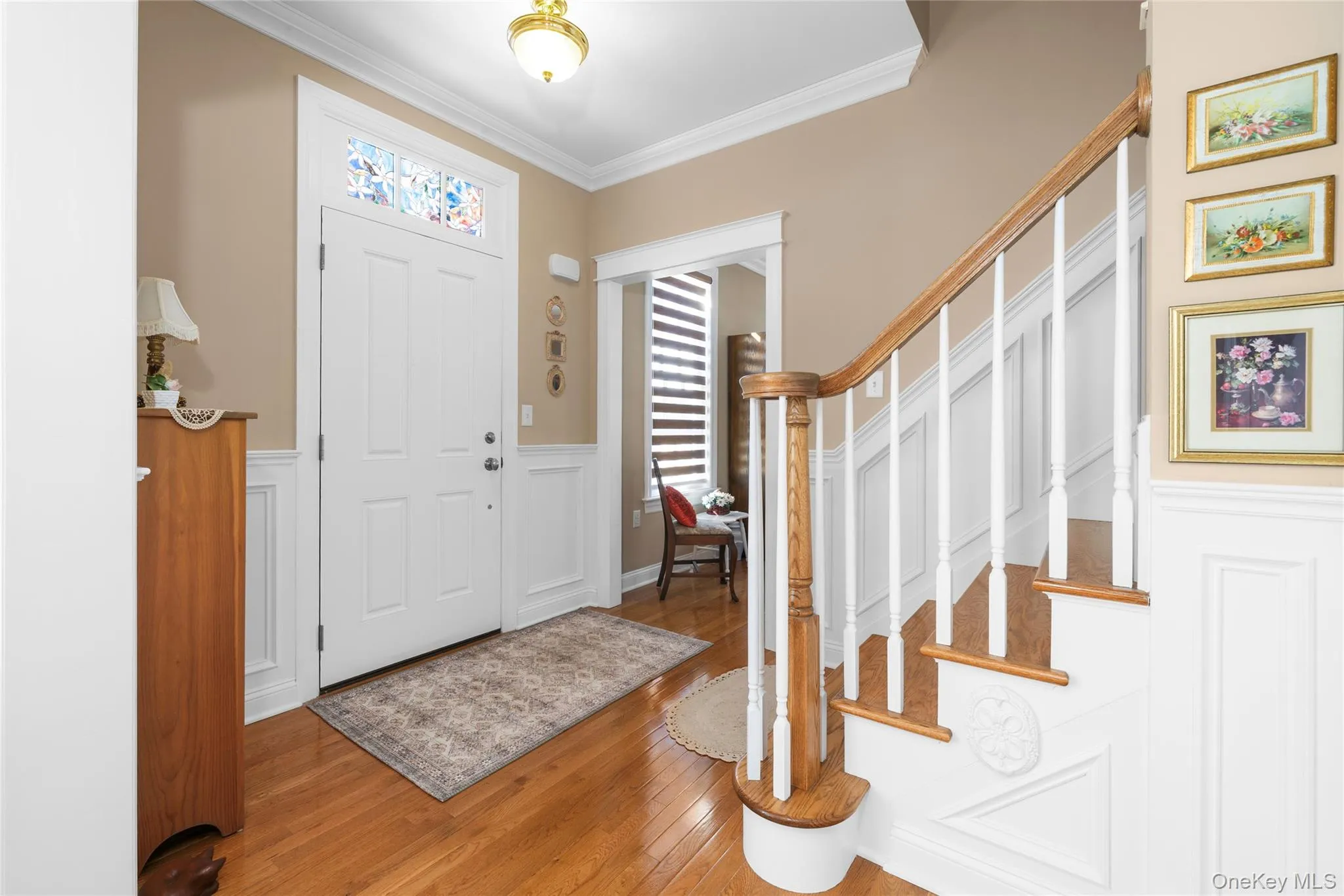 Foyer featuring ornamental molding, wood-type flooring, a wainscoted wall, and a decorative wall Foyer featuring ornamental molding, wood-type flooring, a wainscoted wall, and a decorative wall