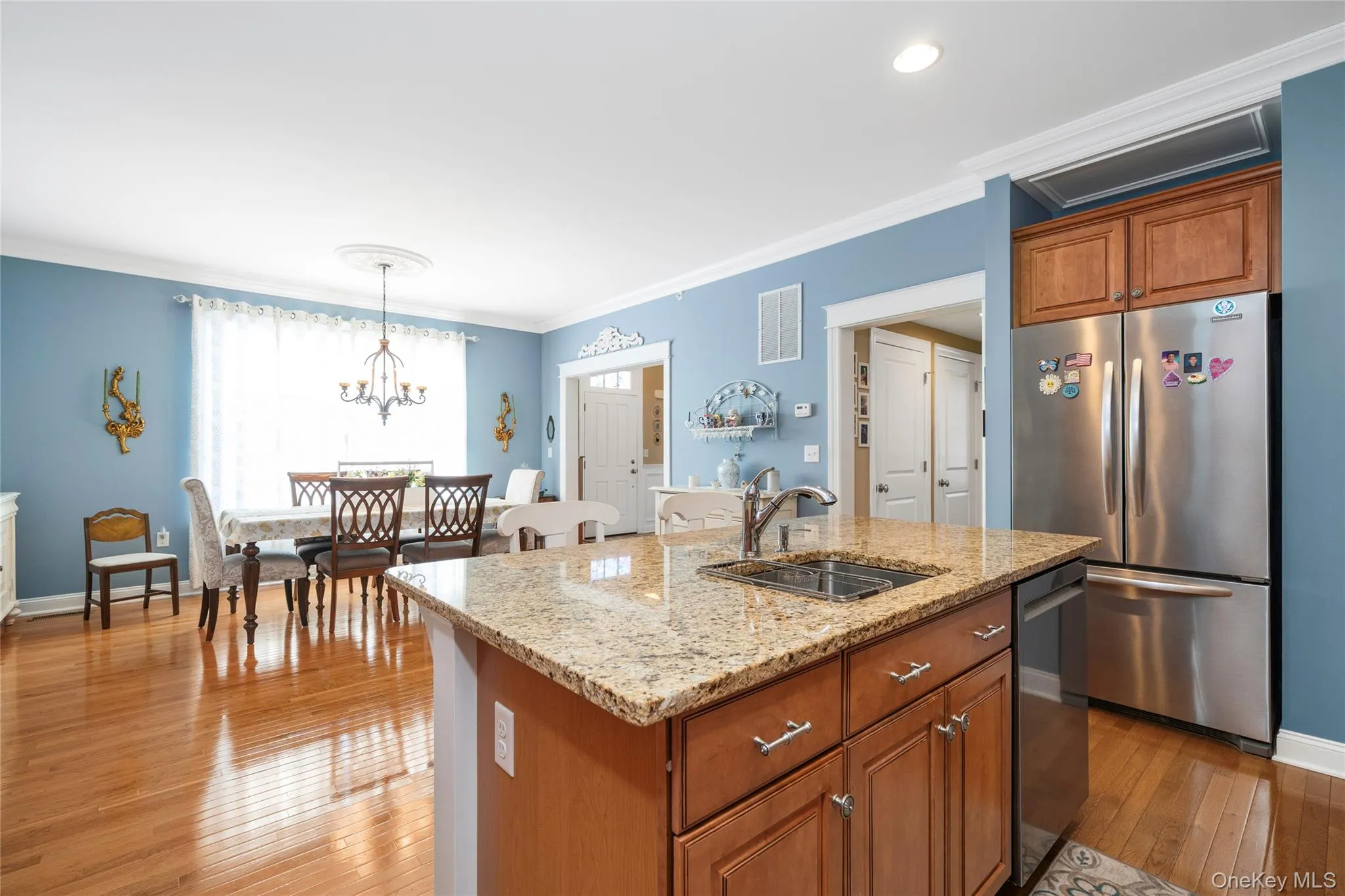 Kitchen featuring wood finish cabinets, stainless steel appliances, light stone counters, light wood-style flooring, and ornamental molding Kitchen featuring wood finish cabinets, stainless steel appliances, light stone counters, light wood-style flooring, and ornamental molding
