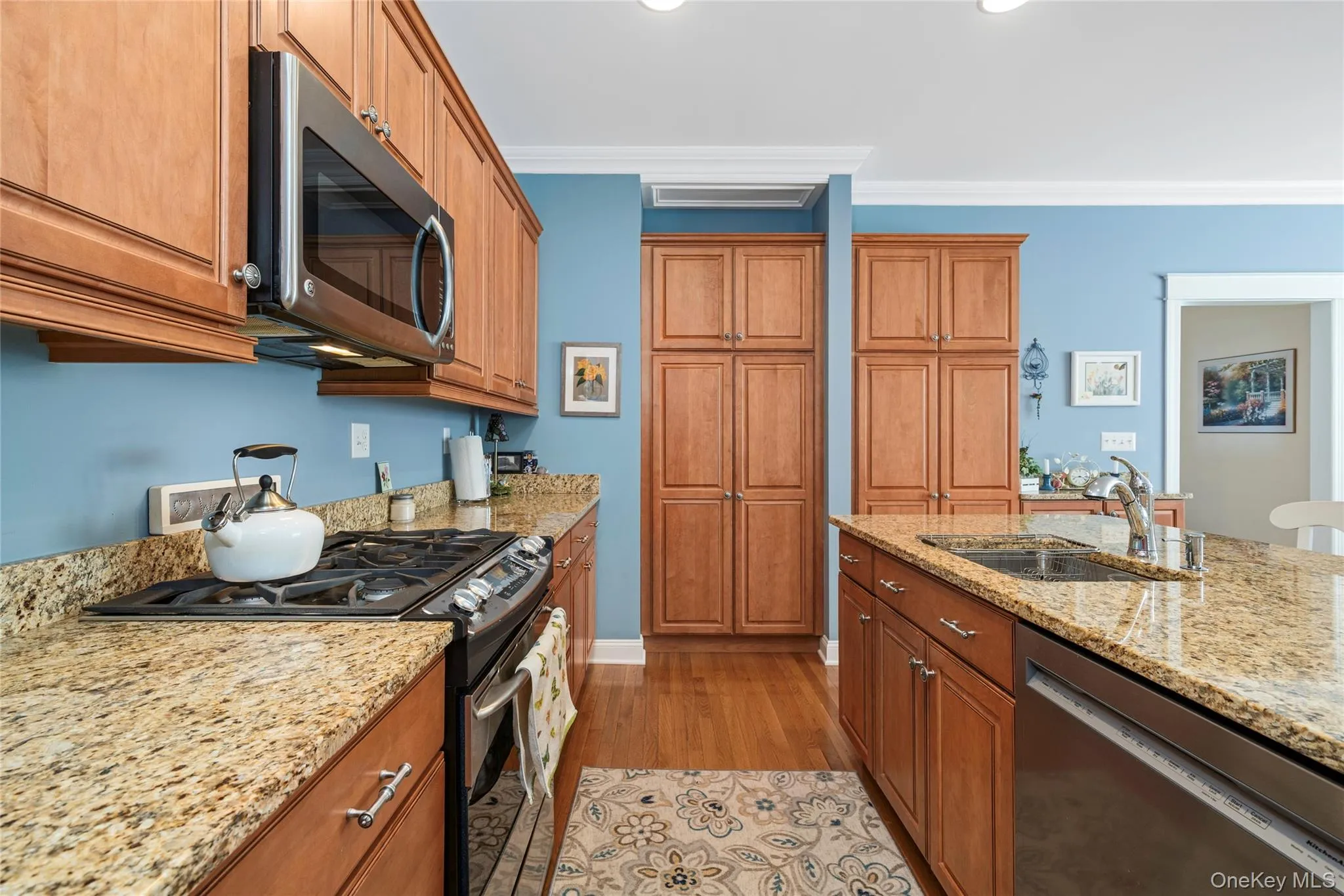 Kitchen featuring stainless steel appliances, wood finish cabinetry, light stone countertops, light wood-style floors, and ornamental molding Kitchen featuring stainless steel appliances, wood finish cabinetry, light stone countertops, light wood-style floors, and ornamental molding